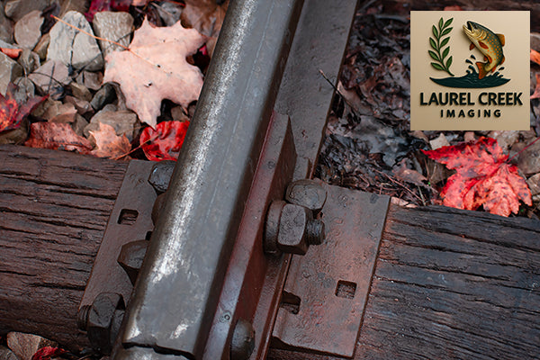 Close-up of a metal rail with gravel and leaves, featuring Laurel Creek Imaging logo.